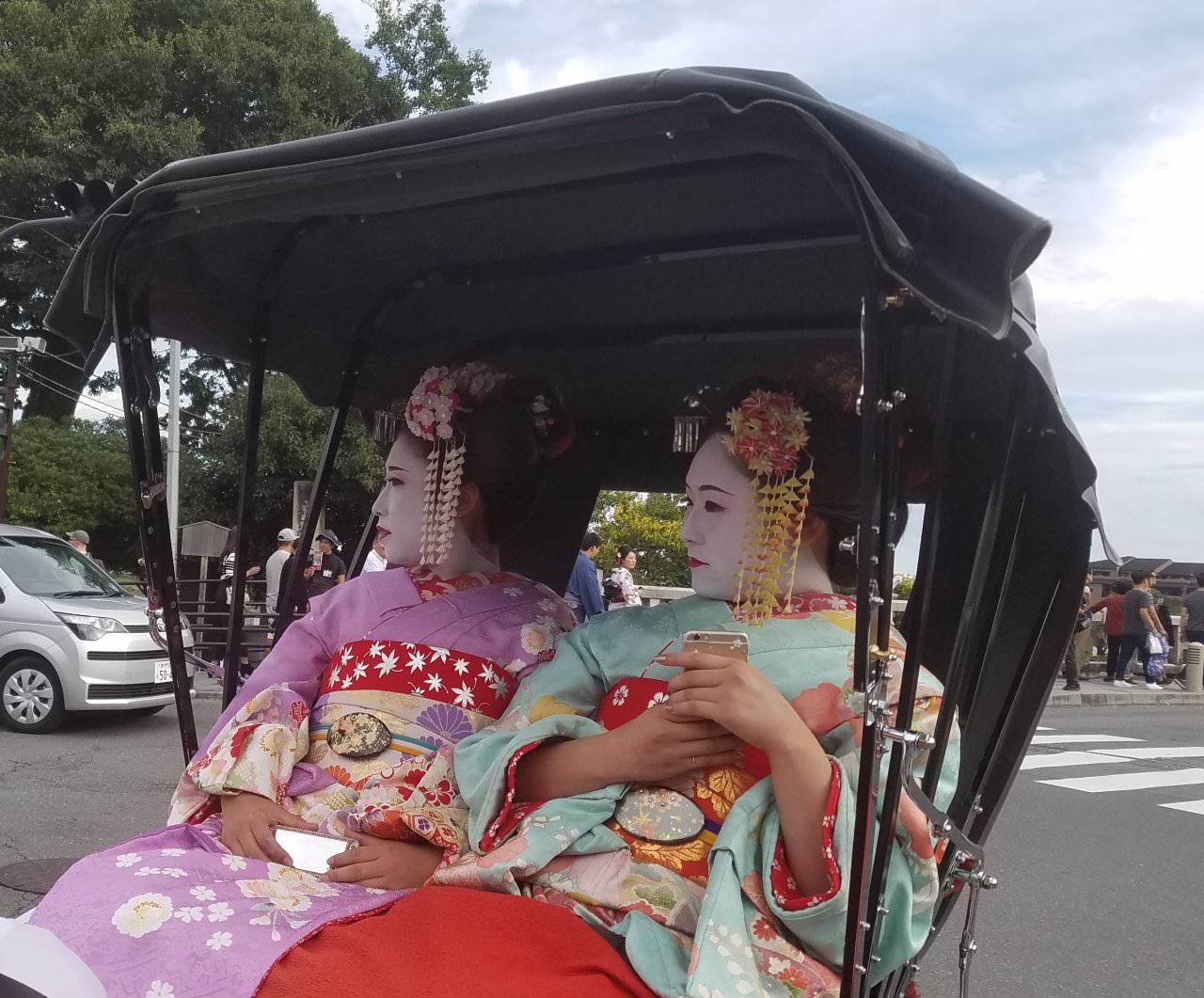 兩位少女穿著日本傳統服裝和打扮，坐上傳統人力車，但手上亦不忘拿著手機，可說是古今時空共融的組合。